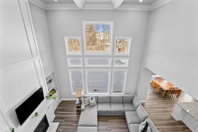 living room featuring baseboards, a fireplace with flush hearth, ornamental molding, beam ceiling, and wood finished floors