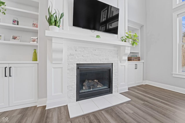 unfurnished living room with a stone fireplace, built in features, baseboards, and wood finished floors