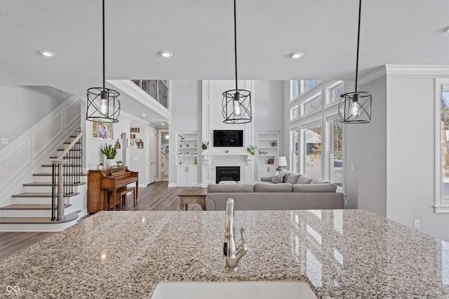 kitchen featuring light stone countertops, crown molding, sink, pendant lighting, and wood-type flooring