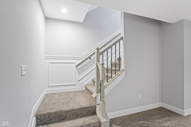 stairway featuring a decorative wall, carpet flooring, and baseboards