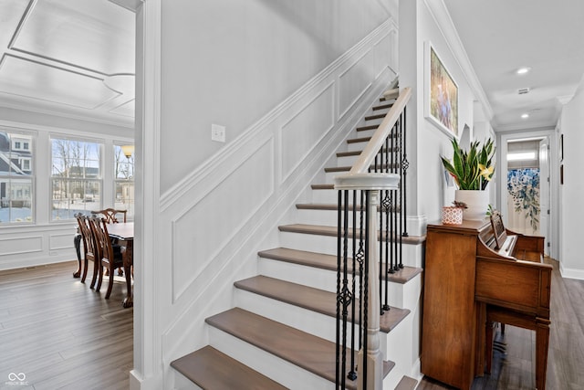 stairs with crown molding, a decorative wall, recessed lighting, and wood finished floors