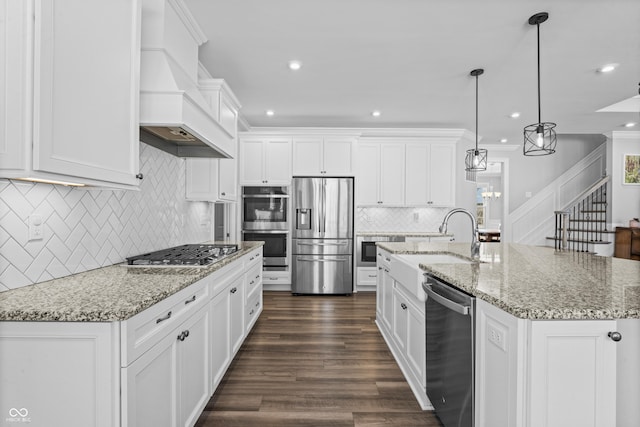 kitchen featuring premium range hood, a kitchen island with sink, ornamental molding, stainless steel appliances, and white cabinetry