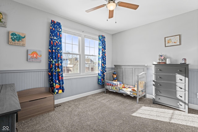 carpeted bedroom featuring a wainscoted wall, visible vents, and a ceiling fan