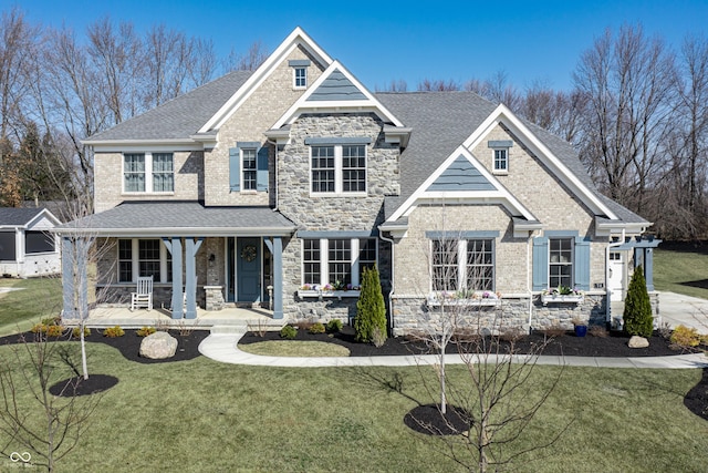 craftsman house featuring stone siding, a porch, a front lawn, and roof with shingles