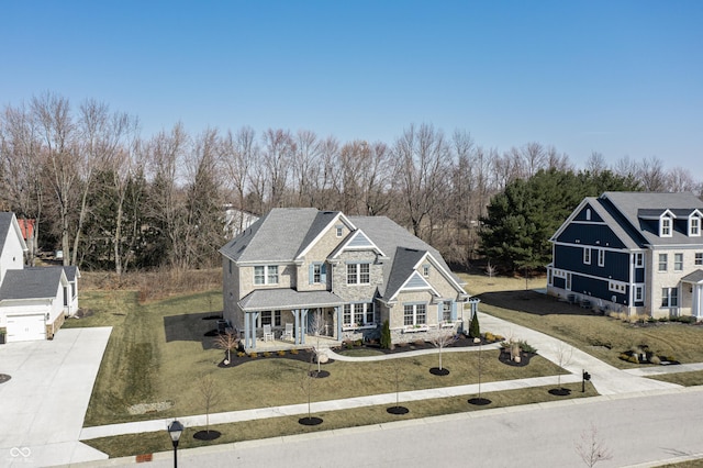 traditional home with a front lawn, a porch, stone siding, and driveway