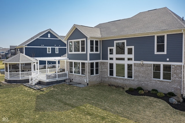 back of property featuring a yard, brick siding, roof with shingles, and a wooden deck