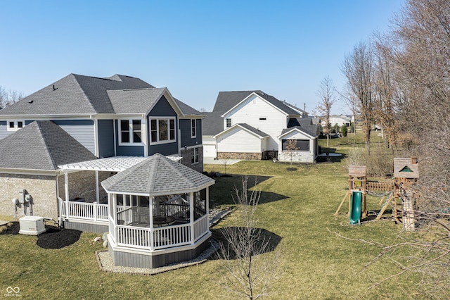 rear view of house with a shingled roof, a playground, and a yard