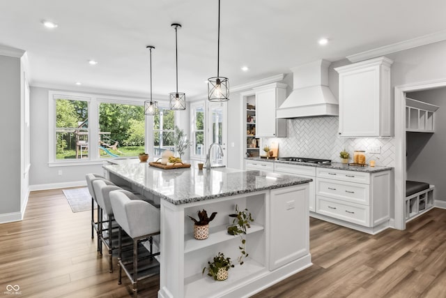 78 Chatham Brook Dr, Westfield, IN 46074 - kitchen featuring premium range hood, white cabinetry, open shelves, decorative backsplash, and a kitchen island with sink