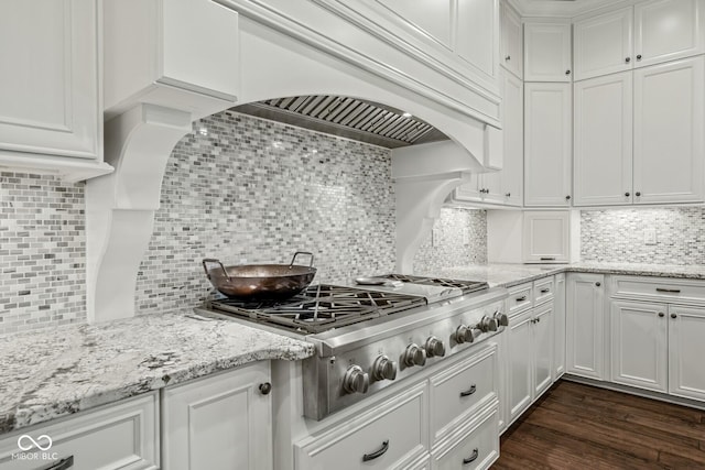 kitchen featuring light stone countertops, custom range hood, white cabinets, decorative backsplash, and stainless steel gas stovetop