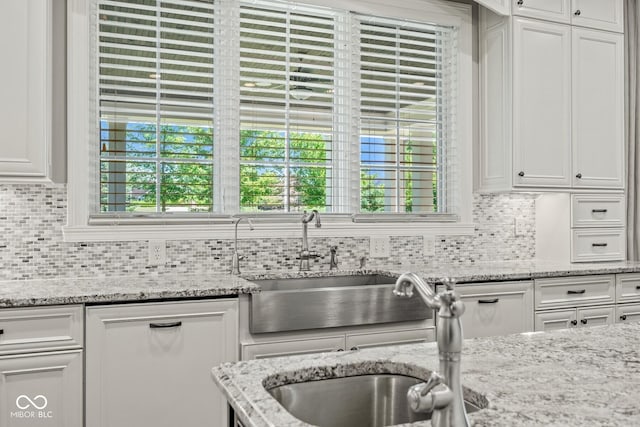 kitchen with white cabinetry, sink, decorative backsplash, and light stone counters