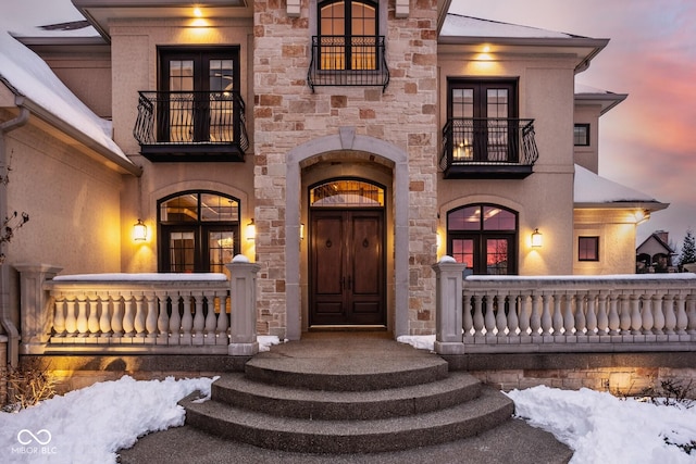 exterior entry at dusk featuring a balcony, covered porch, and french doors