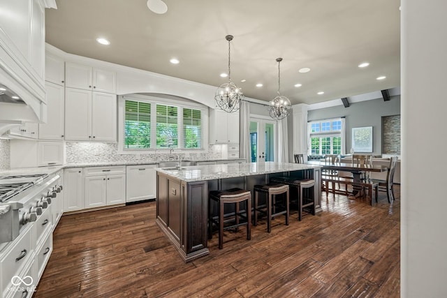 kitchen with light stone counters, a center island, white dishwasher, beamed ceiling, and white cabinets