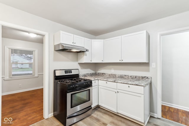 kitchen with light hardwood / wood-style floors, light stone countertops, white cabinetry, and gas stove