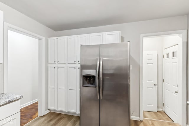 kitchen featuring light stone countertops, white cabinets, stainless steel fridge, and light hardwood / wood-style flooring