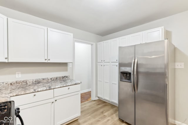 kitchen with light stone countertops, range, stainless steel fridge with ice dispenser, white cabinetry, and light wood-type flooring