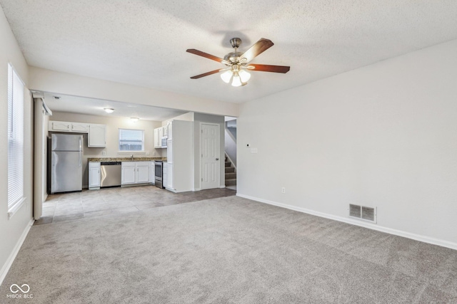 unfurnished living room featuring ceiling fan, light colored carpet, and a textured ceiling