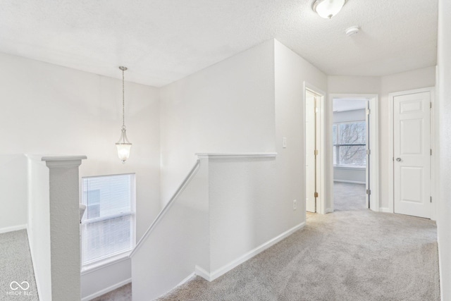 corridor with light colored carpet and a textured ceiling