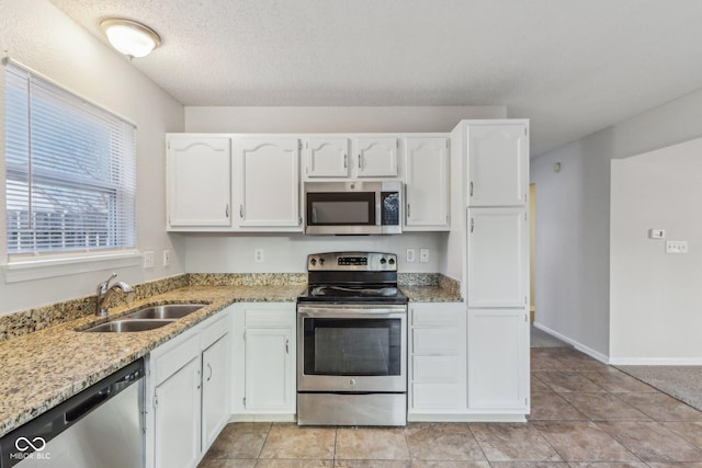 kitchen featuring light stone countertops, appliances with stainless steel finishes, white cabinetry, sink, and light tile patterned floors