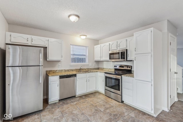 kitchen with sink, white cabinets, a textured ceiling, stone counters, and stainless steel appliances