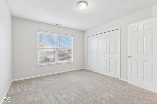 unfurnished bedroom featuring a textured ceiling, a closet, and light carpet