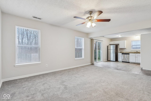 unfurnished living room featuring sink, ceiling fan, light colored carpet, and a textured ceiling