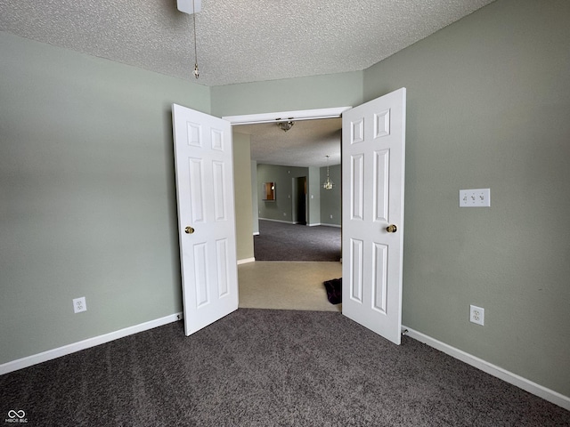 empty room with dark colored carpet, ceiling fan, and a textured ceiling