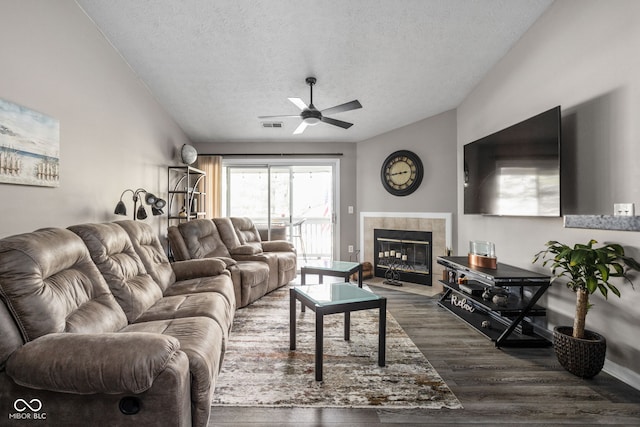 living room featuring dark hardwood / wood-style flooring, a textured ceiling, ceiling fan, lofted ceiling, and a tiled fireplace