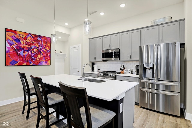 kitchen with a center island with sink, decorative light fixtures, gray cabinets, and stainless steel appliances