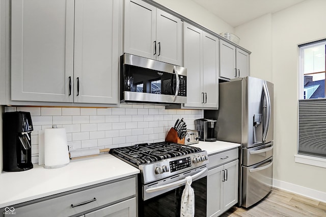 kitchen with backsplash, gray cabinetry, light wood-type flooring, and appliances with stainless steel finishes