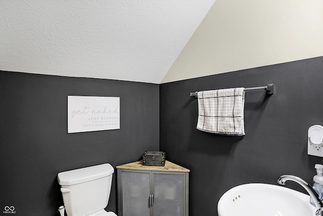 bathroom featuring toilet, a textured ceiling, vaulted ceiling, and sink