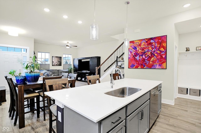 kitchen with gray cabinetry, sink, hanging light fixtures, stainless steel dishwasher, and an island with sink