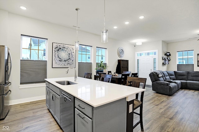 kitchen featuring pendant lighting, gray cabinetry, a kitchen island with sink, sink, and stainless steel appliances