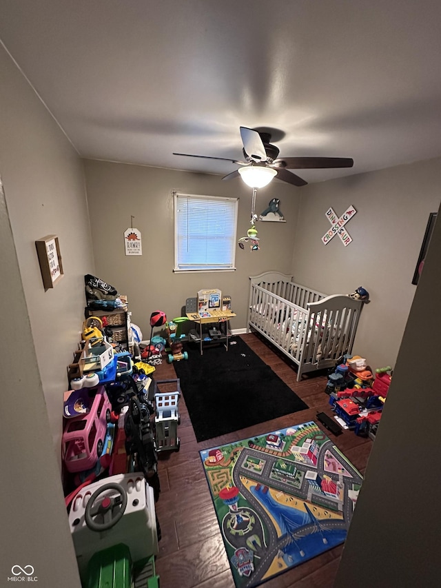 bedroom with ceiling fan, dark wood-type flooring, and a nursery area