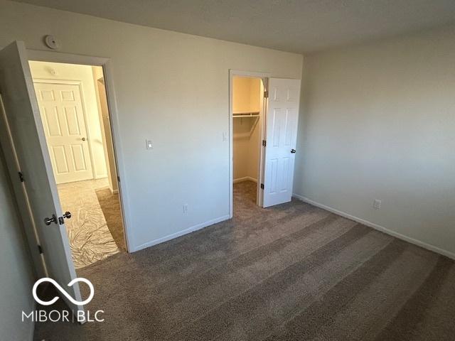 unfurnished bedroom featuring dark carpet, a spacious closet, and a closet