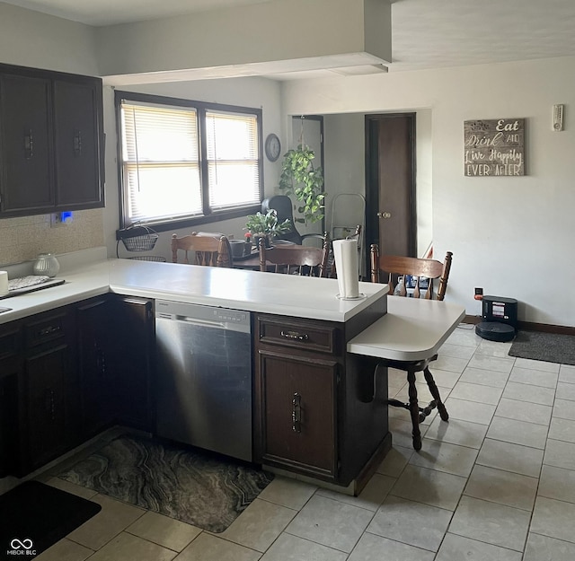 kitchen with dishwasher, kitchen peninsula, light tile patterned floors, dark brown cabinetry, and a breakfast bar area