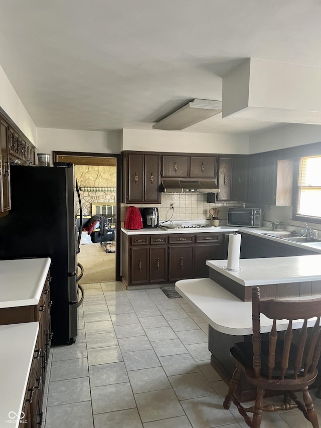 kitchen featuring sink, gas stovetop, tasteful backsplash, refrigerator, and dark brown cabinets