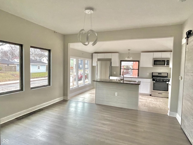 kitchen with pendant lighting, white cabinets, appliances with stainless steel finishes, light hardwood / wood-style floors, and a barn door