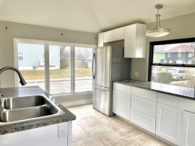 kitchen featuring vaulted ceiling, sink, stainless steel refrigerator, white cabinetry, and hanging light fixtures