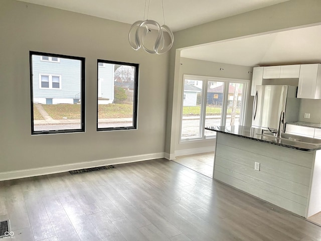 kitchen featuring dark stone countertops, white cabinets, hanging light fixtures, stainless steel refrigerator, and light hardwood / wood-style flooring