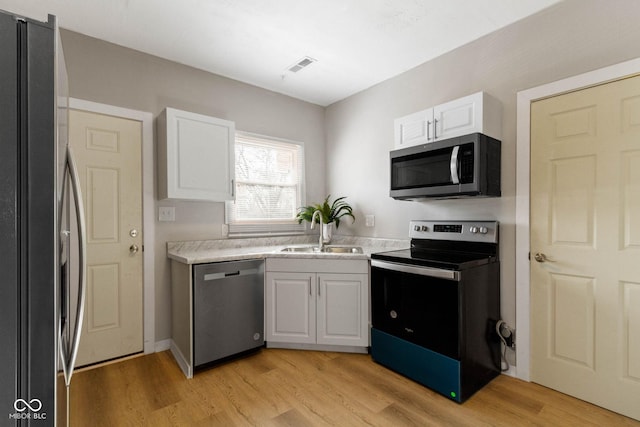 kitchen with appliances with stainless steel finishes, light hardwood / wood-style flooring, white cabinetry, and sink