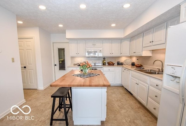 kitchen featuring white appliances, white cabinets, sink, a kitchen island, and butcher block counters