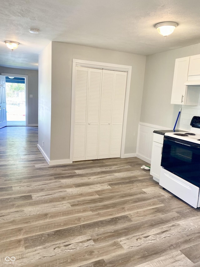 kitchen featuring white electric range, light hardwood / wood-style flooring, white cabinetry, and tasteful backsplash