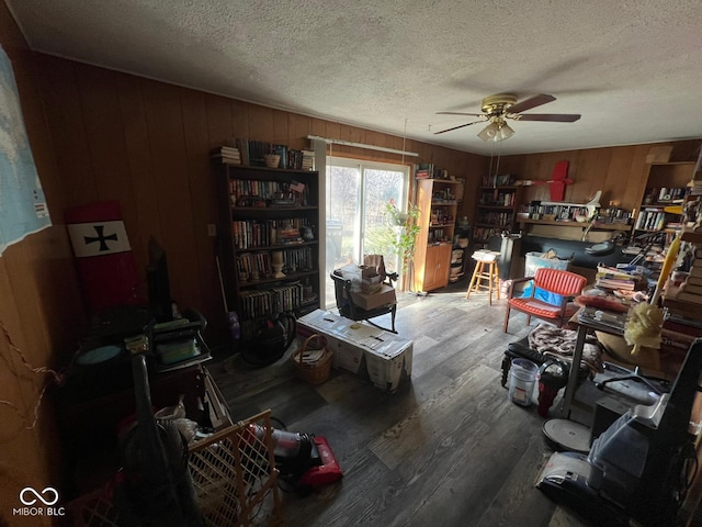 interior space featuring ceiling fan, a textured ceiling, and wooden walls