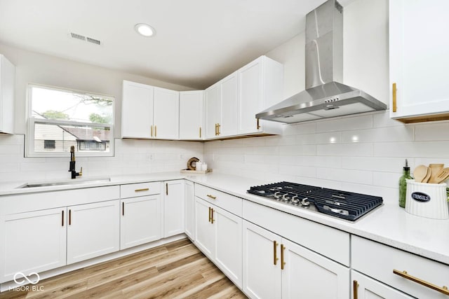 kitchen featuring decorative backsplash, sink, wall chimney range hood, white cabinets, and stainless steel gas stovetop