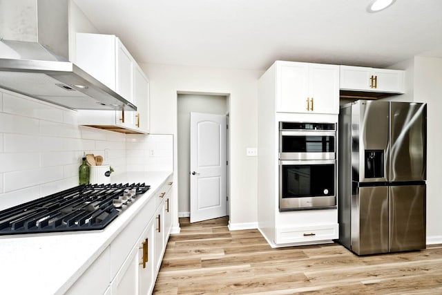 kitchen with light wood-type flooring, tasteful backsplash, wall chimney exhaust hood, stainless steel appliances, and white cabinets