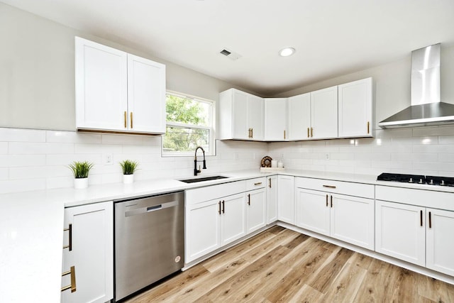 kitchen featuring stainless steel dishwasher, white gas cooktop, sink, wall chimney range hood, and white cabinets