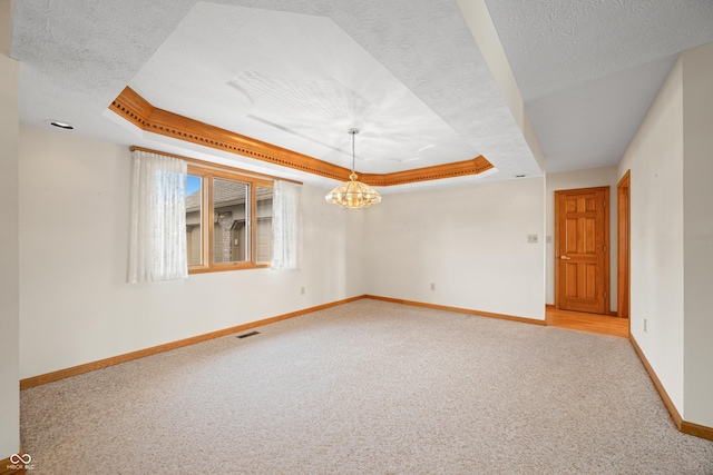 carpeted spare room with a tray ceiling, crown molding, and a chandelier