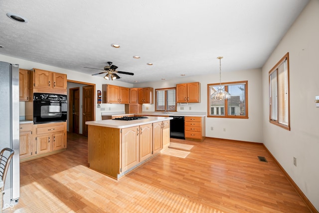 kitchen featuring a center island, black appliances, ceiling fan with notable chandelier, light wood-type flooring, and decorative light fixtures