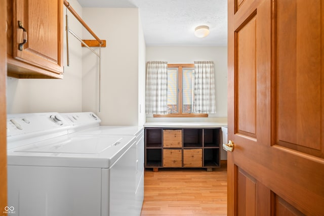 laundry room featuring washer and clothes dryer, cabinets, a textured ceiling, and light hardwood / wood-style floors