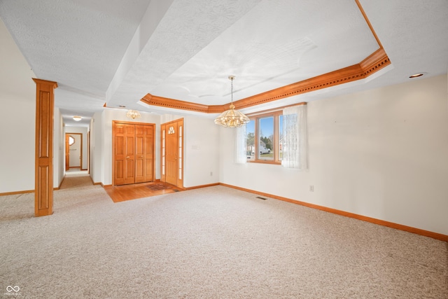 carpeted empty room with a chandelier, a tray ceiling, ornate columns, and ornamental molding